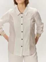 Camisa de lino color blanco con detalles combinados en tonos beige, cuello camisero, cierre frontal con botones oscuros y mangas largas con puños en contraste.