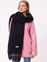 Bufanda de textura suave y voluminosa, color negro, con flecos en los extremos y etiqueta de la marca Rusty cosida en la parte inferior.