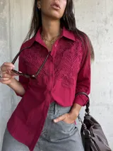 Camisa de color bordó con cuello clásico y cierre frontal de botones. Presenta un diseño distintivo con paneles de encaje bordado en la parte superior delantera, mangas largas con puños y un corte recto.