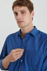 Camisa azul de manga larga con cuello clásico, cierre con botones y bolsillo en el pecho.