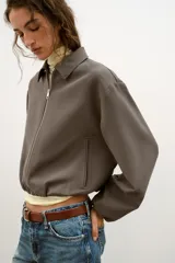 Chaqueta de corte corto y diseño abullonado en color marrón oscuro, con cuello solapa, mangas largas con puños elásticos y cierre frontal con cremallera metálica. Cuenta con bolsillos delanteros de doble vivo.