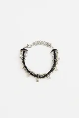 Pulsera de múltiples hilos con cuentas negras de vidrio y cuentas metálicas plateadas, adornada con pequeños dijes colgantes. Cuenta con cierre de mosquetón y cadena de ajuste.