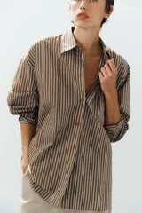Camisa de popelina a rayas marrones, blancas y celestes, con cuello clásico, manga larga, bolsillo frontal de parche y cierre de botones.