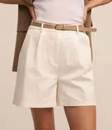Short de sastrería color beige, de corte recto con pinzas delanteras y trabillas en la cintura. Incluye un cinturón de poliuretano a tono con hebilla metálica dorada.