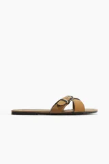 Sandalias planas color tostado, con tiras cruzadas y una hebilla metálica decorativa.