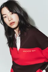 Polo de manga larga con cuello solapa y cierre frontal de botones. Diseño a rayas horizontales anchas en color negro y rojo. Presenta texto bordado en el pecho y parches decorativos en la parte inferior delantera.