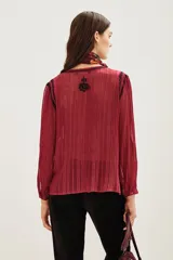 Camisa de manga larga en color negro con tejido semitransparente y detalles de hilos metalizados. Presenta un diseño con bordados florales en tonos tierra, cierre frontal con botones y un lazo decorativo en el cuello.