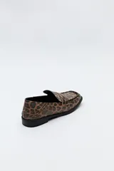 Mocasín de cuero sintético negro con punta cuadrada, detalle de costuras visibles en la capellada y taco bajo.