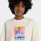 Remera cropped de algodón color crema con mangas cortas y cuello redondo. Presenta un estampado gráfico central que muestra un par de zapatillas deportivas sobre un fondo de bloques de color degradado en tonos amarillo, rosa, morado y azul.