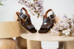 Sandalias de cuero negro con textura de reptil, diseño de punta cuadrada y taco bloque de madera. Presentan tiras cruzadas en el empeine y una hebilla metálica grande decorativa.