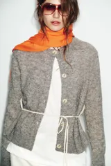 Chaqueta de punto de cuello redondo y manga larga, con diseño combinado que incluye una capa interior en tono crudo. Presenta cierre frontal con botones y puños acanalados.
