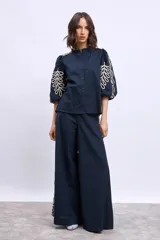 Blusa azul marino con cuello mao, mangas 3/4 abullonadas y bordados en color crema en hombros y mangas.