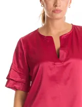 Blusa de satén color verde oliva, con cuello redondo y escote en V. Presenta mangas cortas con tres capas de volados superpuestos.