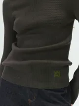 Remera de cuello alto tipo polera, confeccionada en tela rib con textura acanalada y ajuste al cuerpo. Presenta mangas largas y un pequeño bordado distintivo en la parte inferior.