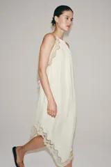 Vestido largo ZARA Woman Collection confeccionado en hilatura de viscosa de color crudo, con cuello halter, tirantes finos, detalles de encaje a tono y bajo asimétrico.