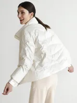 Campera puffer color blanco nacarado, con cuello alto y cierre frontal con botones a presión.