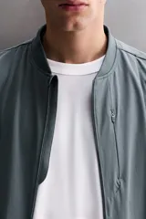 Chaqueta técnica de corte relajado, confeccionada en tejido compacto y elástico. Presenta cuello y puños acabados en rib, cierre frontal con cremallera, bolsillos frontales con cremallera oculta y bajo ajustable con elástico en los laterales.