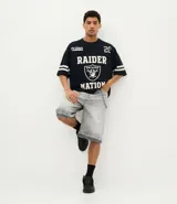 Remera deportiva de corte oversized, color negro, con estampado gráfico en la espalda del equipo Las Vegas Raiders de la NFL. Presenta cuello redondo, mangas cortas con detalles de rayas blancas y logo de la NFL en la parte superior trasera.