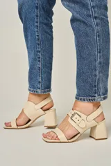 Sandalias de cuero color champagne, con punta cuadrada, tira ancha sobre el empeine y tira al tobillo con hebilla metálica. Taco cuadrado de 7 cm.