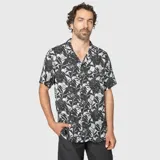 Camisa de manga corta con cuello solapa, confeccionada en viscosa ligera. Presenta un estampado tropical en tonos oscuros y grises, con cierre frontal de botones.
