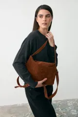 Cartera mediana de gamuza color tostado con detalles en cuero liso al tono. Cuenta con doble asa fija para llevar al hombro y una correa larga desmontable y regulable para usar como bandolera. Posee cierre superior.