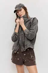 Chaleco de denim color gris deslavado, con cuello camisero, cierre frontal con botones metálicos y costuras decorativas.