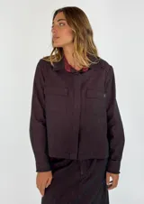 Chaqueta tipo camisa de denim color borgoña, con cuello clásico, manga larga, cierre frontal con botones y bolsillo de parche en el pecho.