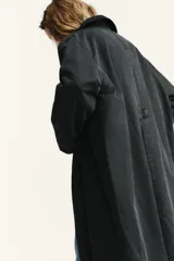 Gabardina larga de tejido con efecto encerado en color gris oscuro. Presenta cuello de solapa en pana, cierre frontal con botones ocultos bajo solapa y bolsillos laterales con botón.