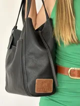 Bolso tote grande de cuero negro con costuras blancas y bolsillo externo con botón.