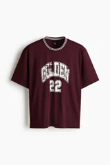 Remera bordó de punto acanalado con corte holgado, cuello redondo con ribete rayado y estampa frontal estilo universitario con la inscripción "GOLDEN" y el número "22" en blanco.