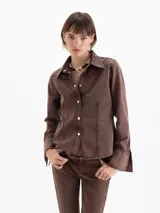 Camisa entallada confeccionada en denim de algodón con lavado marrón chocolate, cuello camisero, cierre frontal con botones y recortes verticales.