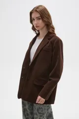 Blazer de pana color marrón, con corte holgado, cuello solapa y cierre frontal con dos botones. Presenta bolsillos laterales con solapa y un bolsillo superior en el pecho.