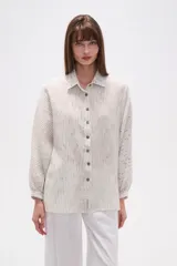 Camisa de corte holgado con cuello clásico y cierre frontal de botones. Presenta mangas largas con puños y un diseño de rayas verticales finas en tonos neutros.