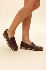 Mocasín de cuero vacuno en color marrón, con diseño bitono que combina texturas lisas y con grabado tipo cocodrilo en el empeine. Cuenta con detalle de estribo clásico y suela plana con vira en contraste.