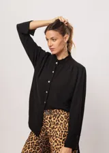 Camisa negra de cuello redondo con frunces y mangas largas con puños abiertos.