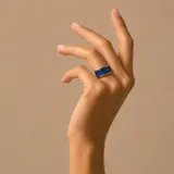 Anillo de banda ancha en tono dorado con tres circonias rectangulares de color azul intenso engastadas en el centro.