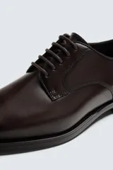 Zapato de vestir estilo Derby color marrón, fabricado en piel con horma redonda, cordones finos y suela con ligero tacón.