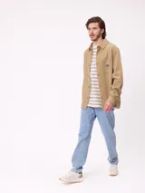 Camisa de gabardina color verde oliva, con cuello clásico, cierre frontal de botones y dos bolsillos frontales con parche. Incluye un pequeño parche con el logo de la marca en el bolsillo izquierdo.