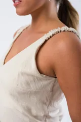 Vestido color beige con escote en V y tirantes finos con detalle fruncido elástico en los hombros. Presenta un corte entallado en el busto con costura horizontal.