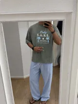 Remera oversize marrón con estampado gráfico frontal en tonos celestes y blancos con la leyenda "Only Fans", palmeras y estrellas.