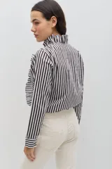 Camisa de algodón con estampado de rayas verticales en color bordó y blanco. Presenta un diseño de manga larga con puños abotonados, cuello camisero y un detalle de volado lateral que recorre el frente desde el cuello hasta el ruedo, acompañando la línea de botones.