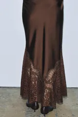 Falda midi de tiro alto confeccionada en tejido satinado color marrón. Presenta un diseño evasé con aplicación de encaje en el lateral y el bajo, y cierre lateral con cremallera oculta.