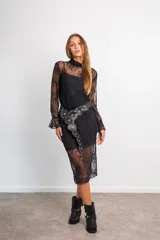 Conjunto de dos piezas compuesto por blusa de encaje semitransparente con cuello alto y mangas largas, y falda midi a juego. Ambas prendas incluyen visos interiores a tono. El diseño presenta un encaje floral delicado en color negro.