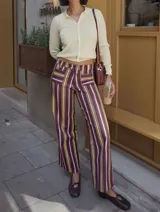 Pantalón de tiro alto con corte recto y caída fluida. Presenta un estampado de rayas verticales en tonos borgoña, chocolate y mostaza, con bolsillos delanteros y pasacintos.
