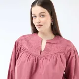 Blusa color rojo con escote en V y cuello mao. Presenta detalles de bordados tonales en el canesú delantero, mangas largas abullonadas y un diseño amplio y fluido.