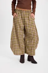 Pantalón de corte holgado con silueta balloon, confeccionado en tela a cuadros verdes y marrones. Presenta cintura elástica con cordón ajustable y bolsillos laterales.