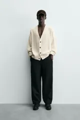 Cárdigan de punto color crema, con cuello pico, manga larga y cierre frontal de botones marrones. Presenta un calce relajado y acabados en rib.