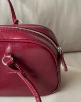 Cartera tipo baguette de cuero sintético color borgoña, con doble asa corta y cierre superior con cremallera.