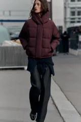 Campera puffer acolchada de color negro, con cuello envolvente, capucha integrada, manga larga, bolsillos laterales ocultos y bajo con elástico. Cierre frontal con botones a presión ocultos por solapa.