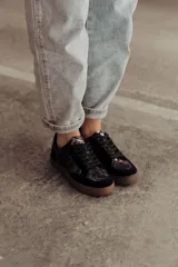 Zapatillas negras con paneles laterales de efecto piel de serpiente metalizado en tonos bronce y negro. Tienen cordones negros y suela de goma color caramelo.